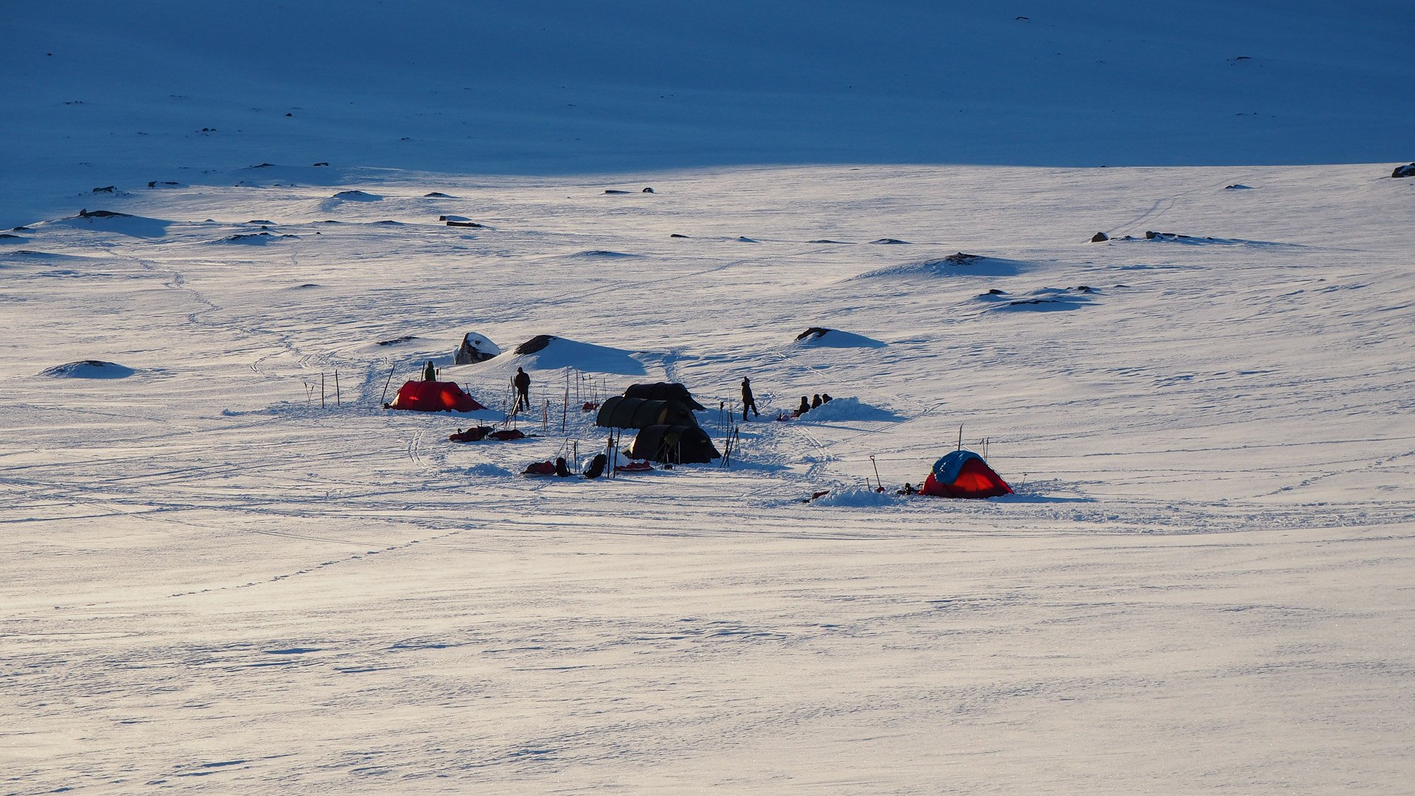 Kuvassa 5 teltan leiri lumisessa laaksossa. 
